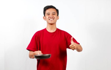 Gülümseyen Asyalı adam kızartma tavasını tutarken başparmağıyla işaret veriyor.