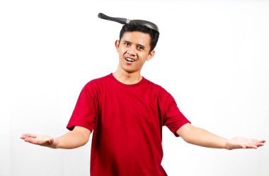 Deli Asyalı adam kollarını açık tutarken kafasına tava takıyor.