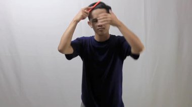 Beyaz arka planda plastik tarakla saç tarayan Asyalı bir adam.