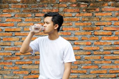 Asyalı bir adamın portresi. Tuğla duvar arkaplanlı şişe suyu içiyor.