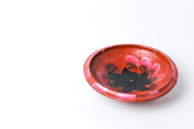 Kırmızı boyayla süslenmiş kilden yapılmış çocuk oyuncağı küçük tabak ve beyaz arka planda izole edilmiş siyah çiçek resmi.
