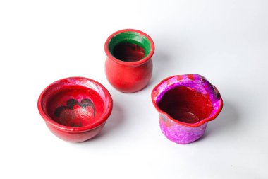 İki tencere ve temiz beyaz bir yüzeye yerleştirilmiş küçük bir sepet de dahil olmak üzere üç renkli el yapımı kil minyatür..