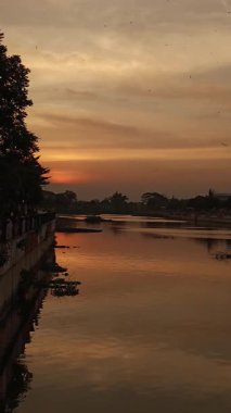 Gün batımı sakin nehir sularını yansıtıyor. Doğanın özgeçmişi, manzarası ve huzurlu anları için mükemmel. Günbatımı renkleri sıcak bir atmosfer yaratır.