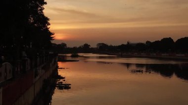 Gün batımı sakin nehir sularını yansıtıyor. Doğanın özgeçmişi, manzarası ve huzurlu anları için mükemmel. Günbatımı renkleri sıcak bir atmosfer yaratır.
