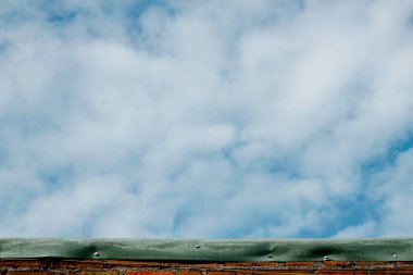 Güzel, berrak gökyüzü, beyaz bulutlar, aşınmış tuğla bir duvarın üzerinde yeşil bir maddeyle yakalanmış..