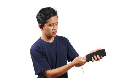 Donanma tişörtü giyen Asyalı adam elinde akıllı telefon ile beyaz arka planda izole edilmiş şarj edilebilir güç kablosu yerleştiriyor. Akıllı telefon şarj kavramı.