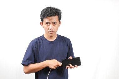 Donanma tişörtü giyen Asyalı adam elinde akıllı telefon ile beyaz arka planda izole edilmiş şarj edilebilir güç kablosu yerleştiriyor. Akıllı telefon şarj kavramı.