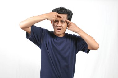 Donanma tişörtü giyen Asyalı adam beyaz arka planda izole edilmiş alnındaki sivilceleri kontrol ediyor.