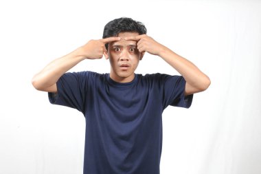 Donanma tişörtü giyen Asyalı adam beyaz arka planda izole edilmiş alnındaki sivilceleri kontrol ediyor.