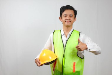 Yeşil yelek giyen, beyaz tişörtlü, şapkalı bir işçinin portresi.