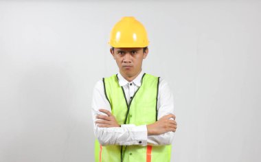 Yelek ve şapkalı bir adam kızgın, kollarını kavuştururken kızgın bir yüz ifadesi sergiliyor..