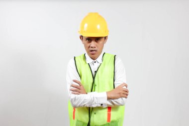 Yelek ve şapkalı bir adam kızgın, kollarını kavuştururken kızgın bir yüz ifadesi sergiliyor..