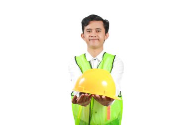 Güvenlik yeleği giymiş gülümseyen inşaat işçisi elinde sarı bir şapka tutuyor. Beyaz arka planda izole edilmiş. Adam dost canlısı ve cana yakın görünüyor.