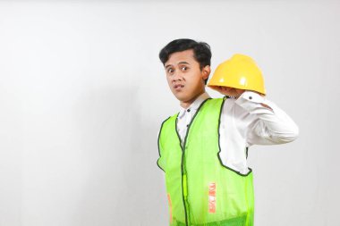 Güvenlik yeleği giyen bir inşaat işçisi ya da mühendis ve elinde şaşırmış ya da kafası karışmış bir ifadeyle sarı bir şapka var..
