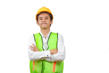 Kendine güvenen genç bir inşaat işçisinin portresi muhteşem bir bina inşa etmek için kollarını kavuşturuyor. Yeşil bir yelek, beyaz gömlek ve beyaz bir arka planda izole edilmiş maden şapkası vardı..