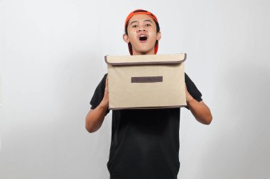 Heyecanlı genç adam beyaz arka planda sürpriz bir ifadeyle teslimata hazır bir paketi tutuyor.