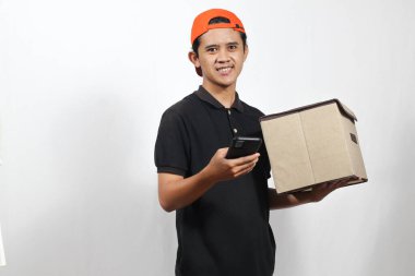 Asyalı kurye yüzünde mutlu bir ifadeyle cep telefonunu kontrol ederken bir paket teslim ediyor. Modern dağıtım hizmeti sunar.