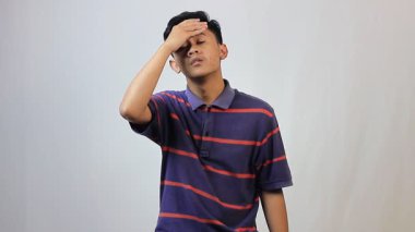 Mor ve kırmızı çizgili gömlek giyen Asyalı bir adam beyaz arka planda baş ağrısı çekiyor.