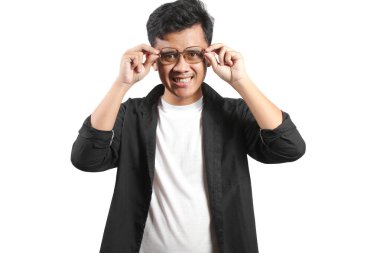 Gülümseyen genç bir adam siyah gömlek ve beyaz bir tişört giyerken klasik gözlüklerini ayarlıyor..