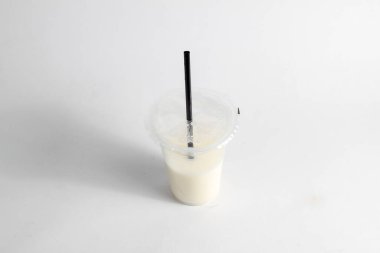 Plastik bardakta siyah pipetli soya sütü içeceği. İçki beyaz bir arka plana karşıdır.
