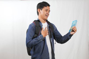 Sırt çantalı genç Asyalı öğrenci elinde para tutarken gülümsüyor ve minnet duyuyor. Ekonomi, başarı, başarı ve finansal özgürlük kavramı.