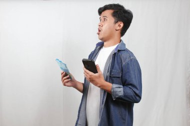 Asyalı adam elinde para yelpazesi ve akıllı telefon ile beyaz arka planda ekstra maaş primi bulduğuna şaşırdı.