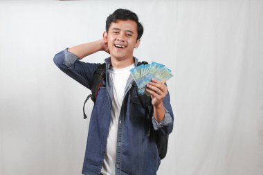 Kot gömlek ve çanta giyen Asyalı bir adam Rupiah 'ın parasını elinde tutarken kafası karışmış bir şekilde mali planlama yapmadan yüzünü kaşıyordu.