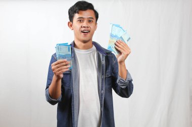 Kot gömlek giyen Asyalı adam elinde para yelpazesi beyaz arka planda izole edilmiş neşeli bir ifade tutuyor.