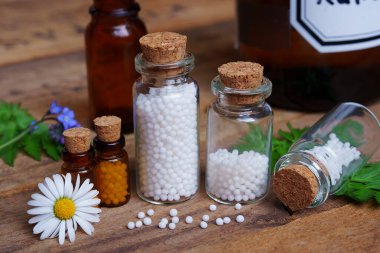 Tahta masada, küreyle dolu tıbbi cam şişeler. Yapraklar ve çiçeklerle dekore edilmiş. Homeopati konzepti.