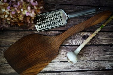 A wooden spatula, a metal grater, and a garlic bulb on a rustic wooden surface. clipart