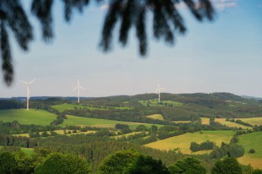 Berrak bir gökyüzünün altındaki yuvarlanan tepelerde rüzgar türbinleri olan manzaralı bir yer..