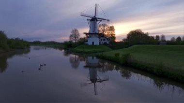 Hollanda 'da bir yel değirmeni gökyüzünde dikiliyor, çarpıcı bir günbatımı tarafından çerçevelenmiş, ikonik yapısını vurguluyor.
