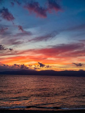 Bulutlu gökyüzü ve denizdeki kızıl gün batımı