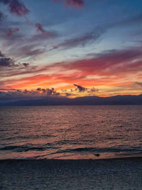Bulutlu gökyüzü ve denizdeki kızıl gün batımı