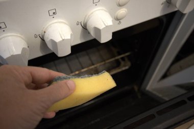 Fırını temizlerken sünger tutan bir elin yakın çekimi. Temizlik ve bakımı vurguluyor.