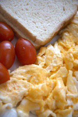 Çırpılmış yumurta, vişneli domates ve bir dilim ekmek. Yakın çekim, sağlıklı ve dengeli bir kahvaltı sunar..