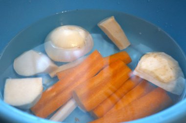 Havuç, maydanoz kökü, kohlrabi, kereviz kökü ve suyla dolu mavi kasede soğan da dahil olmak üzere taze soyulmuş sebzeler..