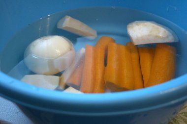 Havuç, maydanoz kökü, kohlrabi, kereviz kökü ve suyla dolu mavi kasede soğan da dahil olmak üzere taze soyulmuş sebzeler..