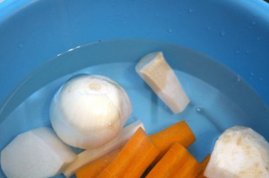 Havuç, maydanoz kökü, kohlrabi, kereviz kökü ve suyla dolu mavi kasede soğan da dahil olmak üzere taze soyulmuş sebzeler..