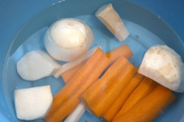 Havuç, maydanoz kökü, kohlrabi, kereviz kökü ve suyla dolu mavi kasede soğan da dahil olmak üzere taze soyulmuş sebzeler..