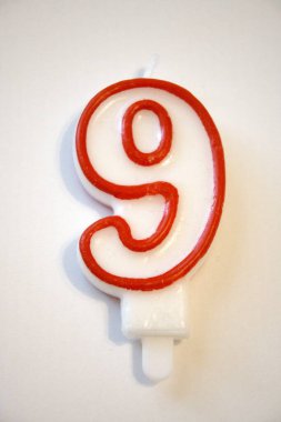 Tek sayılı dokuz doğum günü mumu yakından çekilmiş, beyaz bir arka planda izole edilmiş. Doğum günü kutlamaları ve yıldönümleri için ideal..