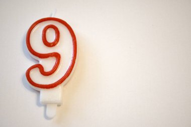 Tek sayılı dokuz doğum günü mumu yakından çekilmiş, beyaz bir arka planda izole edilmiş. Doğum günü kutlamaları ve yıldönümleri için ideal..