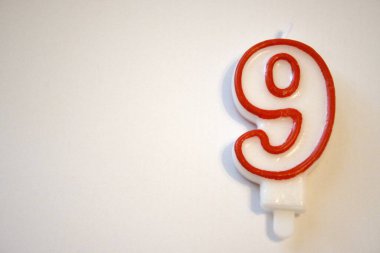 Tek sayılı dokuz doğum günü mumu yakından çekilmiş, beyaz bir arka planda izole edilmiş. Doğum günü kutlamaları ve yıldönümleri için ideal..