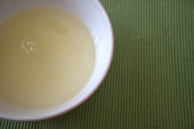 Yeşil bir yüzeye yerleştirilmiş çiğ yumurta beyazıyla dolu küçük cam kase..