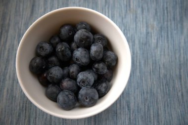 Mavi tekstil üzerine yerleştirilmiş beyaz bir kâse içinde olgun yaban mersinlerinin yakın plan çekimi..