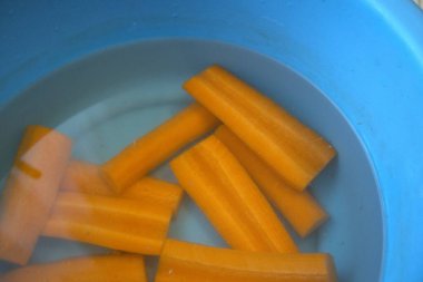 Taze uzamış havuç dilimleri mavi bir kasenin içine daldırılmış sağlıklı yiyecek hazırlama konsepti..