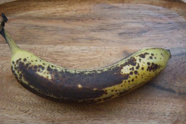 Tahta masa yüzeyinde kahverengi kabuklu olgun bir muzun yakın çekimi, uzay konseptini kopyala.