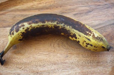 Tahta masa yüzeyinde kahverengi kabuklu olgun bir muzun yakın çekimi, uzay konseptini kopyala.