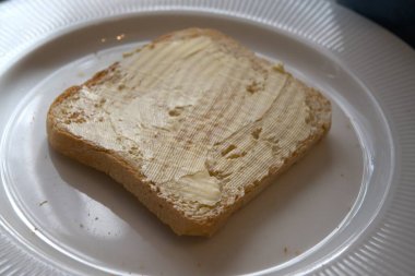 Beyaz tabakta margarin ile yayılmış kızarmış ekmek diliminin yakın görüntüsü..