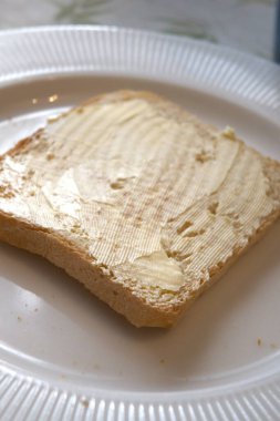 Beyaz tabakta margarin ile yayılmış kızarmış ekmek diliminin yakın görüntüsü..